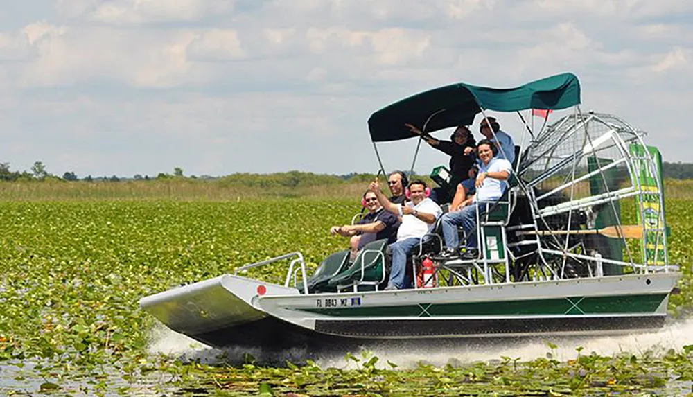 A group of passengers are enjoying a ride on an airboat gliding through a marshy area