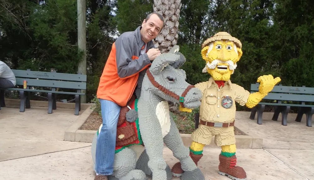 A person is posing with life-sized Lego sculptures of a dinosaur and a park ranger