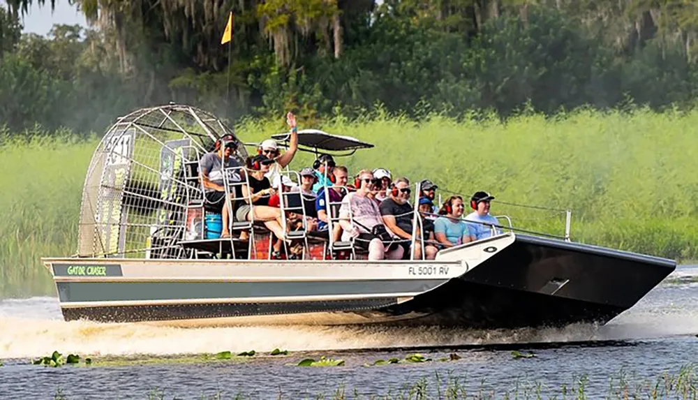 A group of tourists enjoy a ride on an airboat likely in a swamp or marshland with one person excitedly raising their hand