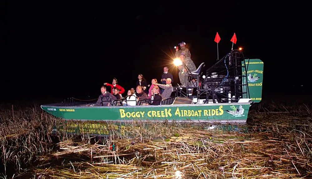 A group of passengers wearing life vests are enjoying a night-time airboat ride through a marshy area with a guide spotlighting the surroundings
