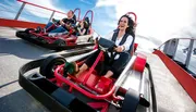 Three people are enjoying a thrilling ride on a go-kart track under a clear blue sky.