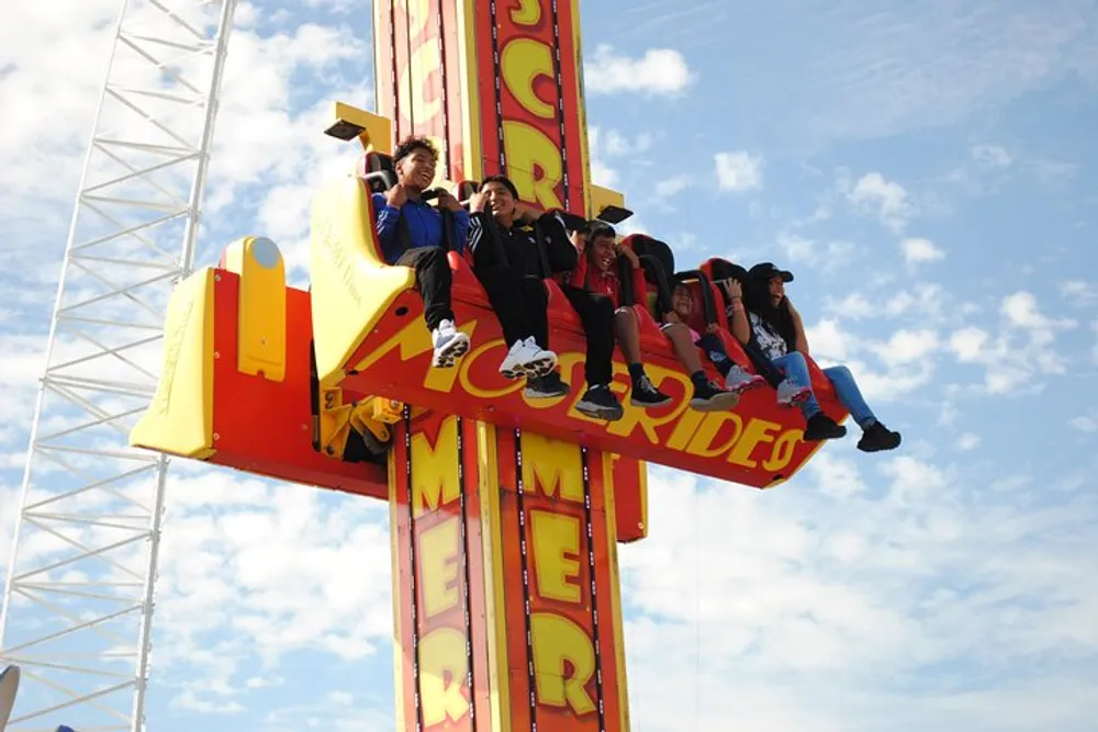 A group of people are experiencing a thrilling drop ride at an amusement park under a blue sky with scattered clouds