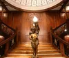 An ornate bronze statue of a figure holding a lamp stands at the base of a grand wooden staircase with detailed craftsmanship