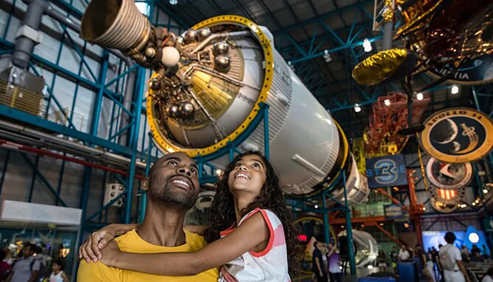 A man and a child joyfully look up at a large space exhibit inside a museum
