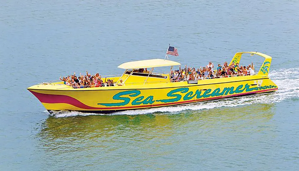 A large group of people are enjoying a ride on a vibrant yellow boat named Sea Screamer as it speeds across the water