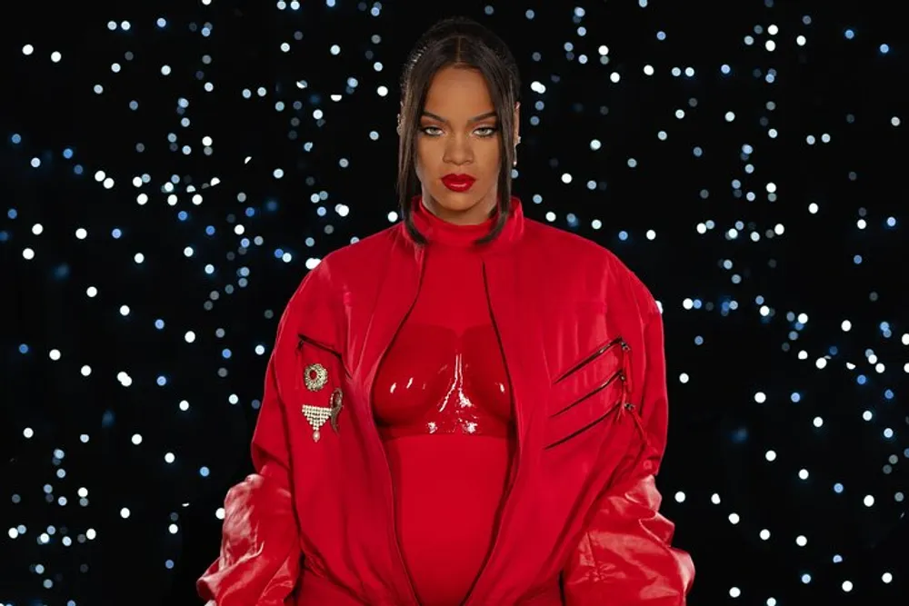 The image shows a person wearing a glossy red outfit with matching lipstick posing confidently against a backdrop dotted with numerous small white lights