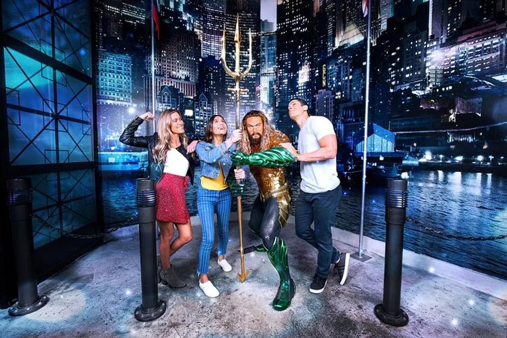 Three visitors are posing playfully with a life-sized statue of the superhero Aquaman at what appears to be a themed attraction or wax museum