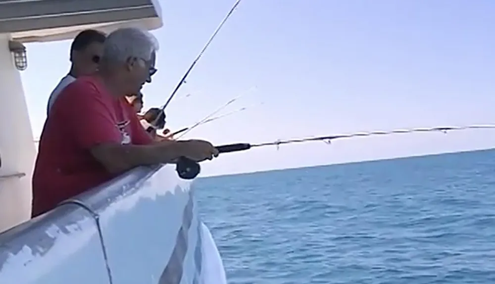 Two individuals are fishing from the side of a boat on a calm blue sea