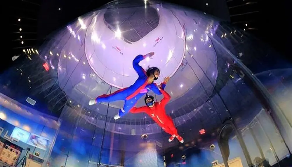 Two people are indoor skydiving in a vertical wind tunnel seemingly enjoying an exhilarating flying experience