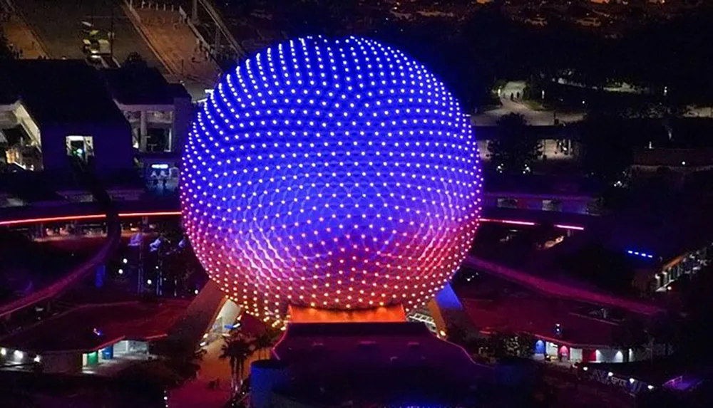 A nighttime aerial photo captures the illuminated geodesic sphere of Spaceship Earth the iconic attraction at Epcot in Walt Disney World