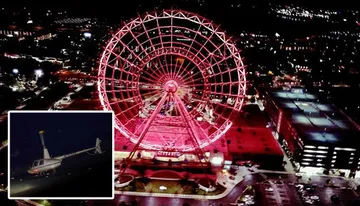 The image shows a vibrant, illuminated Ferris wheel at night, providing a striking focal point in an urban landscape.