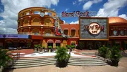 This image shows the iconic facade of a Hard Rock Cafe with its signature guitar and logo, under a clear blue sky.