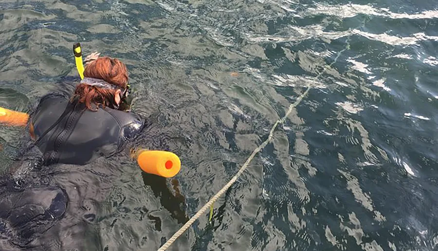 A person in a wetsuit is snorkeling in the ocean, tethered to a bright yellow flotation device.