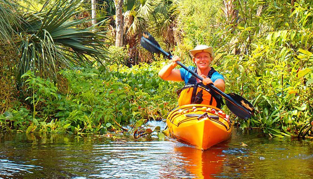 A person with a broad smile is kayaking along a river surrounded by lush greenery