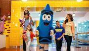 A family is enjoying a fun outing with two people in crayon costumes at a colorful, playful location.