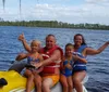 A family of four is posing with thumbs up on a yellow jet ski in a large body of water surrounded by trees under a partly cloudy sky