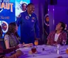 An individual in a NASA astronaut suit is leaning over a table to interact with smiling people seated around it