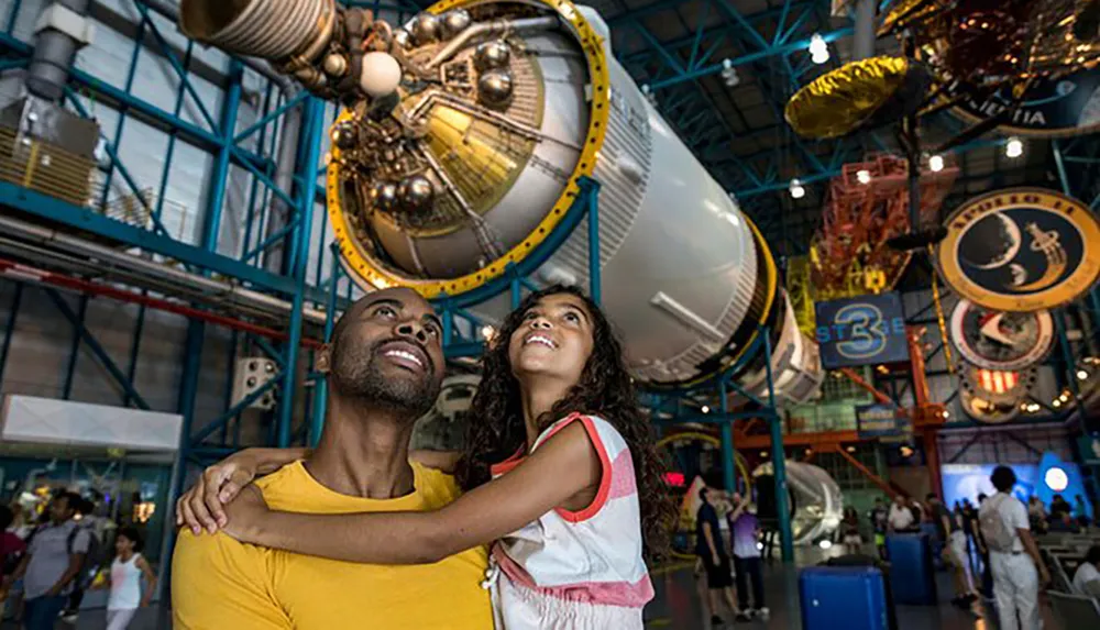 A man and a young girl likely father and daughter are smiling and looking up in wonder at space-related exhibits in a museum