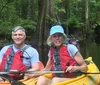 Two people are smiling while kayaking together on a calm river surrounded by greenery