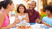 A family is enjoying a meal together outdoors with smiles and a sense of togetherness.
