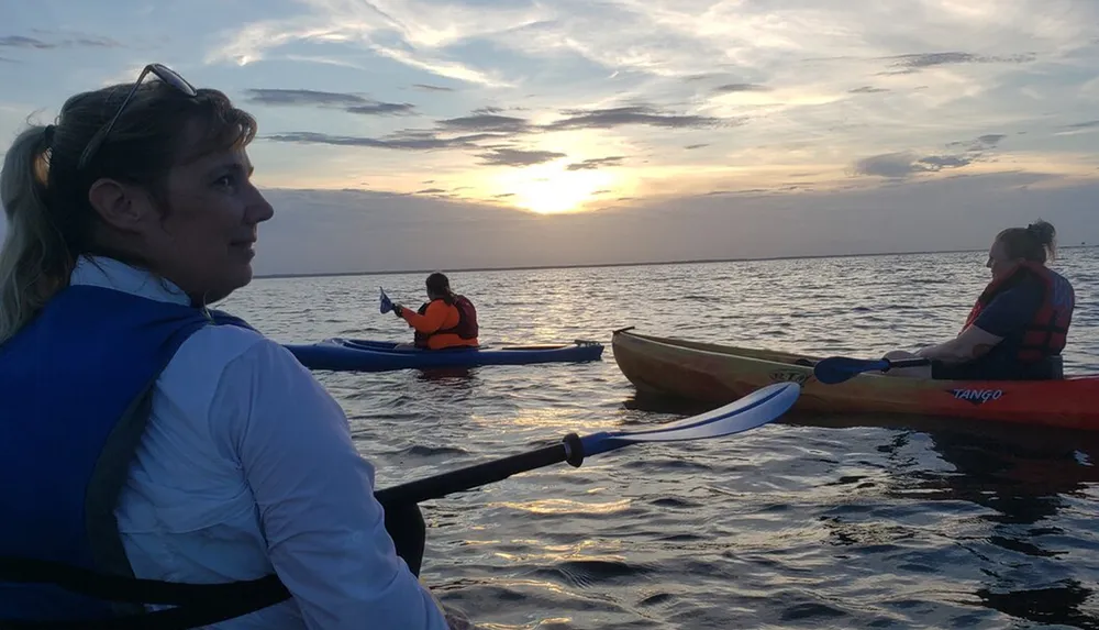 A group of people are kayaking on calm waters with the sun setting in the background