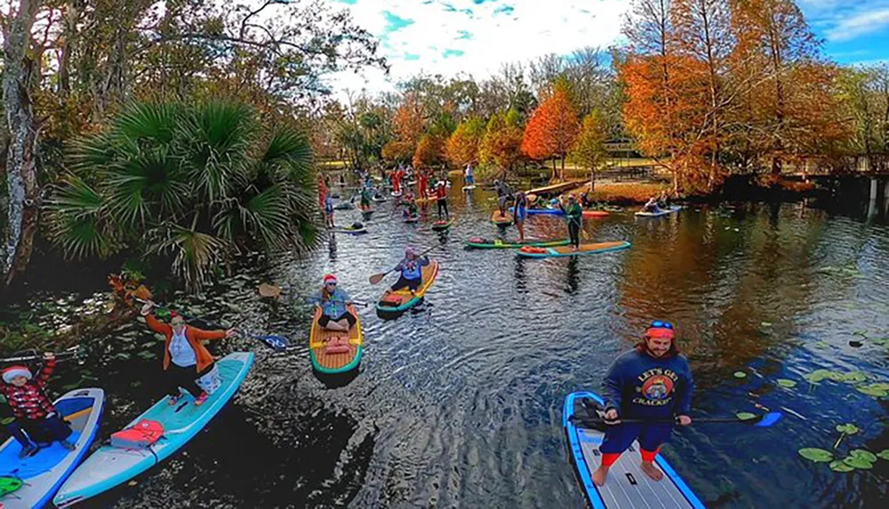 A group of people in festive attire are enjoying paddleboarding and kayaking on a scenic river surrounded by autumn foliage