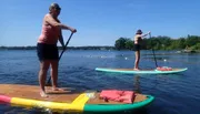 Two people are stand-up paddleboarding on a calm lake on a sunny day.