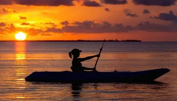 A person kayaks in tranquil waters against the backdrop of a vibrant sunset.