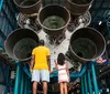 A smiling man and a young girl look up in awe at a spacecraft exhibit in a space museum