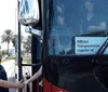 A group of passengers is boarding a red city bus at a stop with cars passing by on the adjacent lane