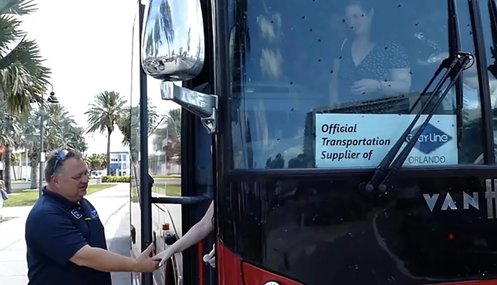 A bus driver is opening the door of a large black bus with a reflection in the doors glass creating an illusion of a woman standing inside the bus