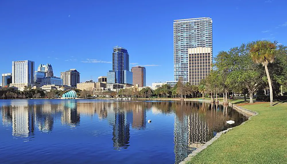 The image depicts a scenic view of a modern city skyline reflected in a tranquil body of water framed by lush greenery and a clear blue sky