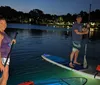 A silhouette of a person paddleboarding on a tranquil sea illuminated by underwater lights against a dramatic sunset sky