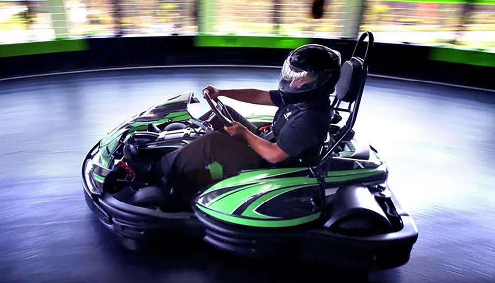 A person wearing a helmet is driving a go-kart on an indoor track conveying a sense of speed and motion