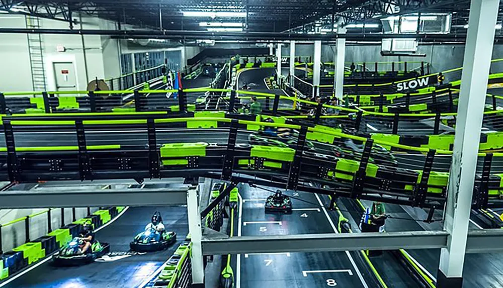 The image shows an indoor go-kart track bustling with activity and featuring multiple levels of brightly colored racing lanes