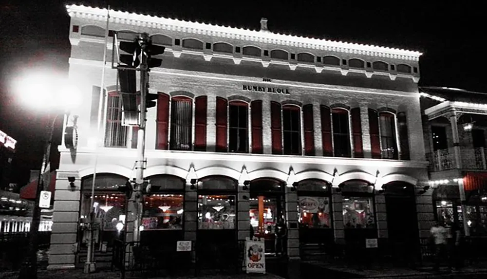 The image displays a two-story historic brick building with arched windows and a sign that reads HUMBY BLOCK at night illuminated by street lights with a OPEN neon sign visible at the ground level establishments