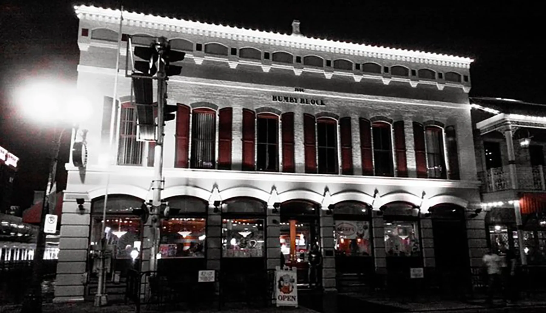 The image displays a two-story historic brick building with arched windows and a sign that reads HUMBY BLOCK at night, illuminated by street lights, with a OPEN neon sign visible at the ground level establishments.