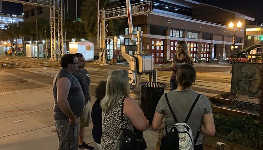 A group of people is gathered around a giant sculpture of a toothbrush at night in an urban setting