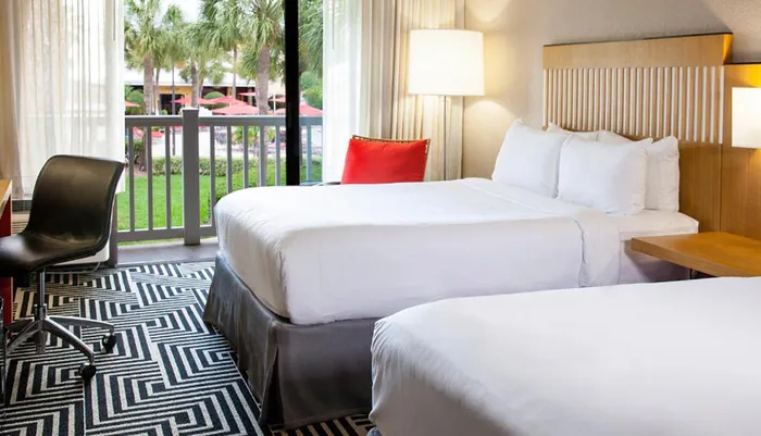 This is an image of a neatly arranged hotel room with two beds featuring crisp white linens and a view to the outdoors