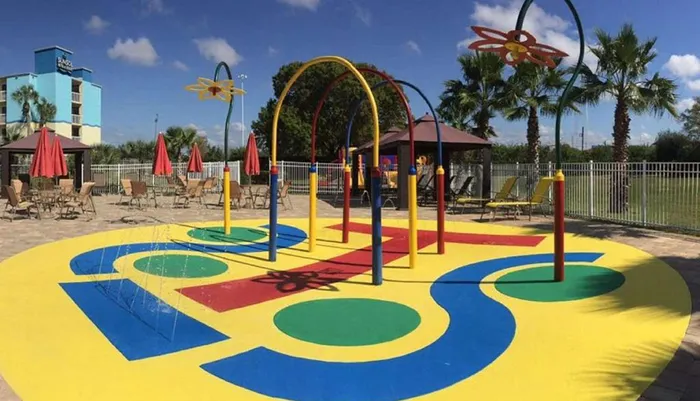 This is a colorful outdoor childrens splash pad with playful water features and seating areas under a sunny sky