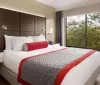 The image depicts a neatly arranged hotel room with a large bed modern furnishings and a window with a view of trees