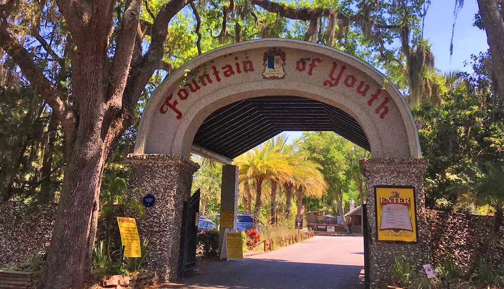 The image shows the entrance arch to the Fountain of Youth with lush trees and a clear sky in the background