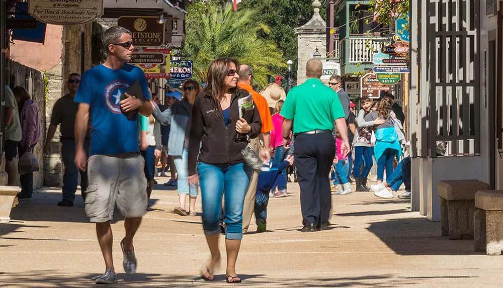 People stroll through a lively street lined with shops and restaurants on a sunny day