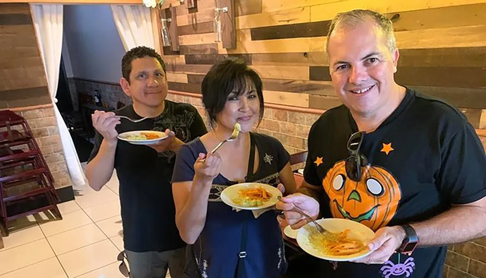 Three people are smiling and posing for a photo while holding plates of food with one of them about to take a bite