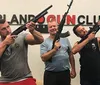 Three men are posing with firearms in front of a wall that has ORLANDO GUN CLUB written on it