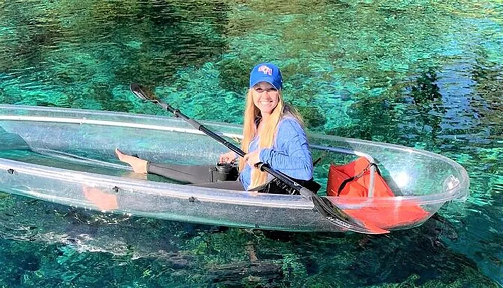 A person is smiling while sitting in a transparent kayak over clear turquoise water