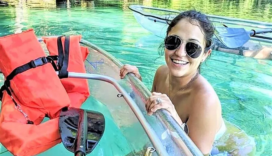 A smiling person is enjoying a kayak adventure on clear, turquoise waters.