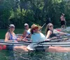 A group of smiling people are enjoying kayaking and paddleboarding on a sunny day in clear water with lush greenery in the background