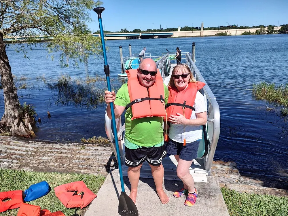 Two people wearing life jackets are standing by a dock ready for a kayaking adventure