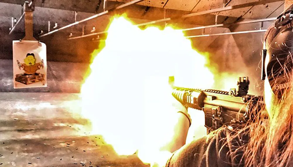A person is firing a rifle on a shooting range with a bright muzzle flash visible
